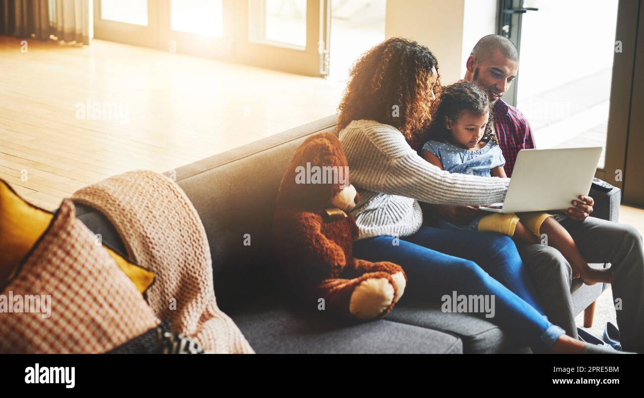 Chi meglio imparare da mamma e papà. Una adorabile bambina e i suoi genitori che usano un notebook insieme sul divano di casa. Foto Stock