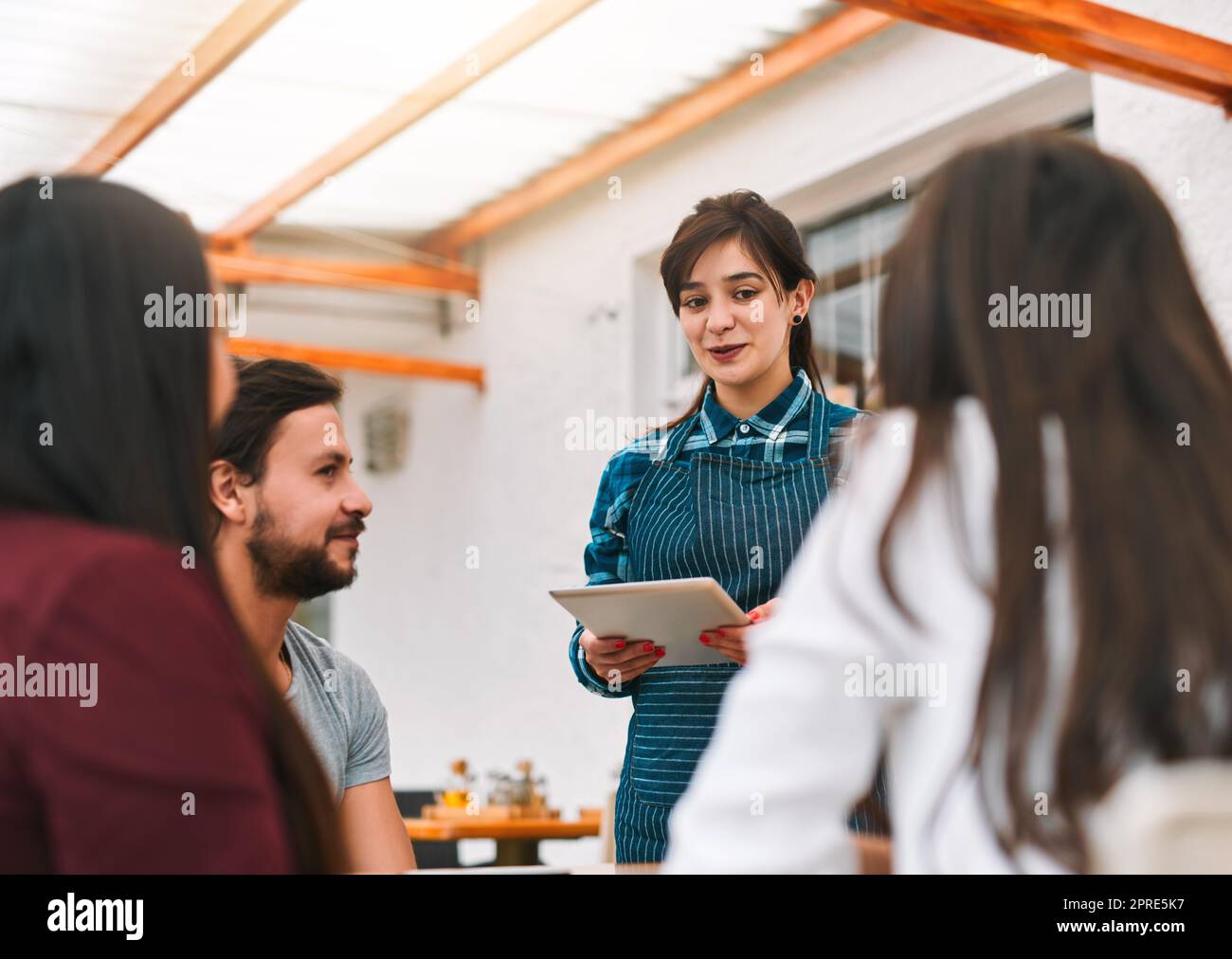 Cosa avrete oggi? un gruppo allegri giovani colleghi d'affari che ordinano cibo e bevande da un cameriere mentre si siedono in un ristorante. Foto Stock