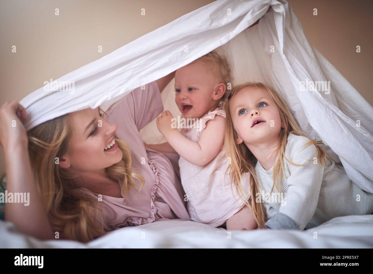 Famiglia, la chiave per la felicità. Una famiglia adorabile di tre persone che giocano sotto un lenzuolo sul letto a casa. Foto Stock