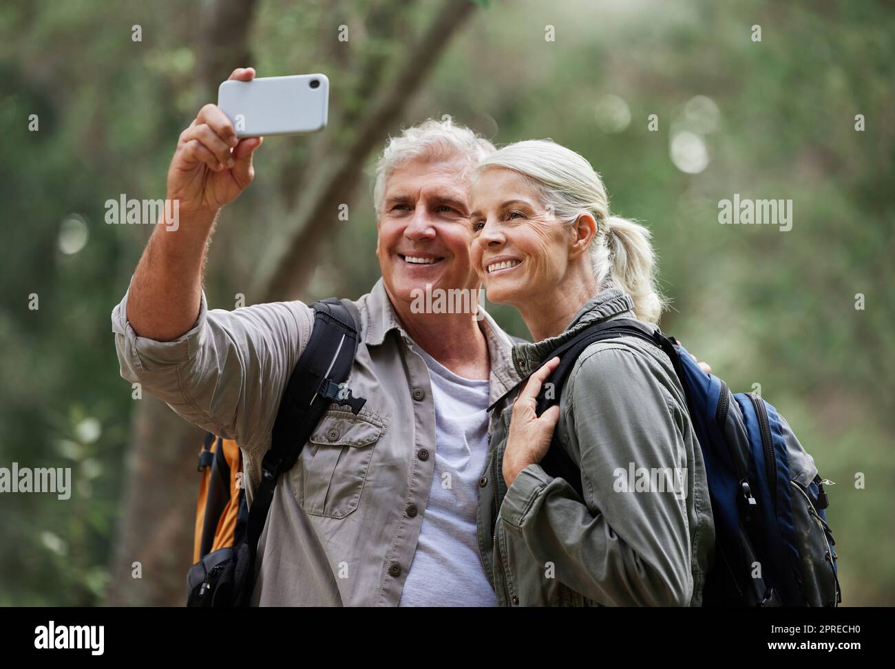 Ritratto di una coppia caucasica anziana sorridente e scattando un selfie con uno smartphone in una foresta durante un'escursione all'aperto. Uomo e moglie che mostrano af Foto Stock
