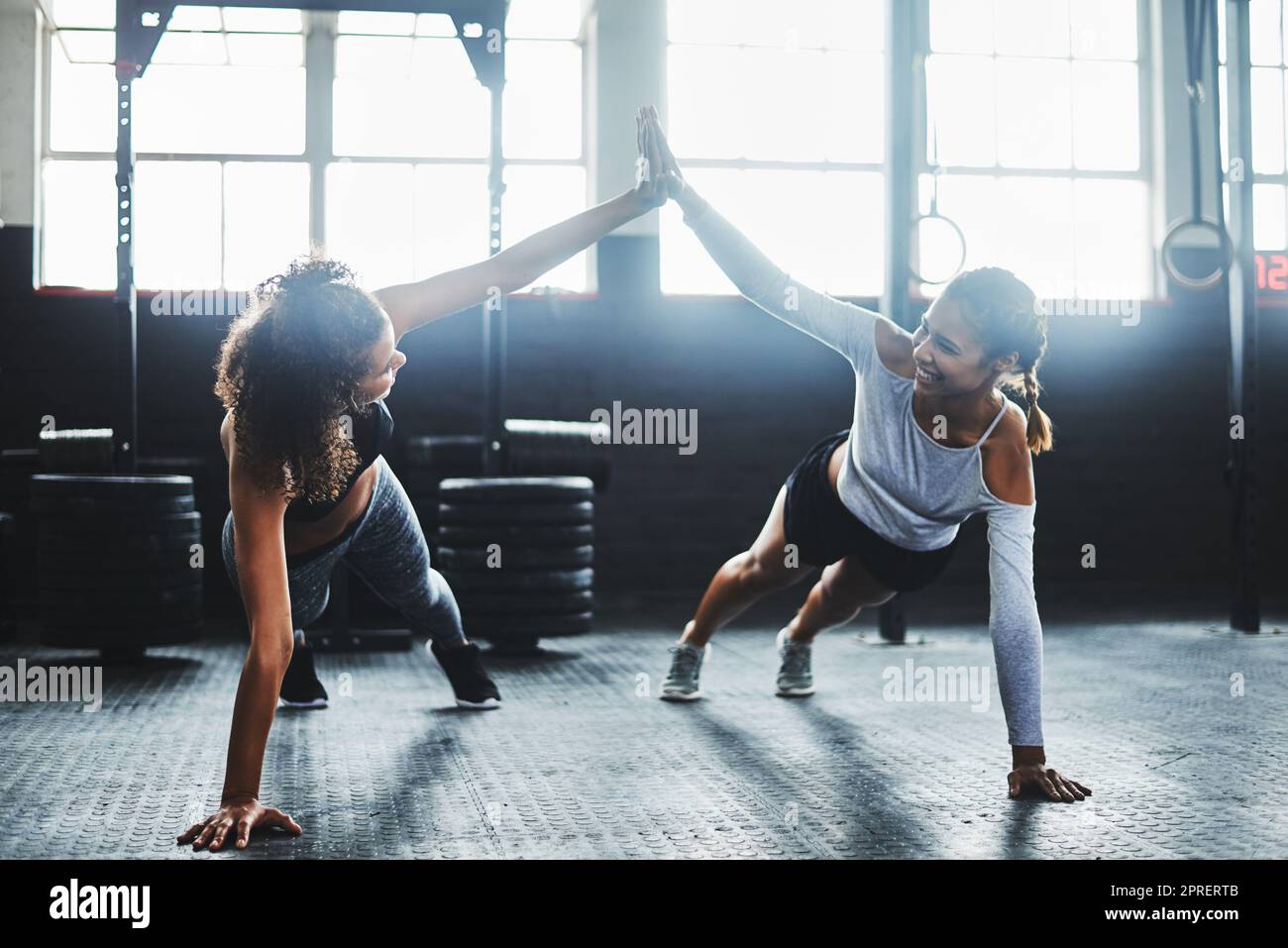 La motivazione fa la differenza: Due giovani donne si danno a vicenda un alto cinque mentre fanno i push up in palestra. Foto Stock