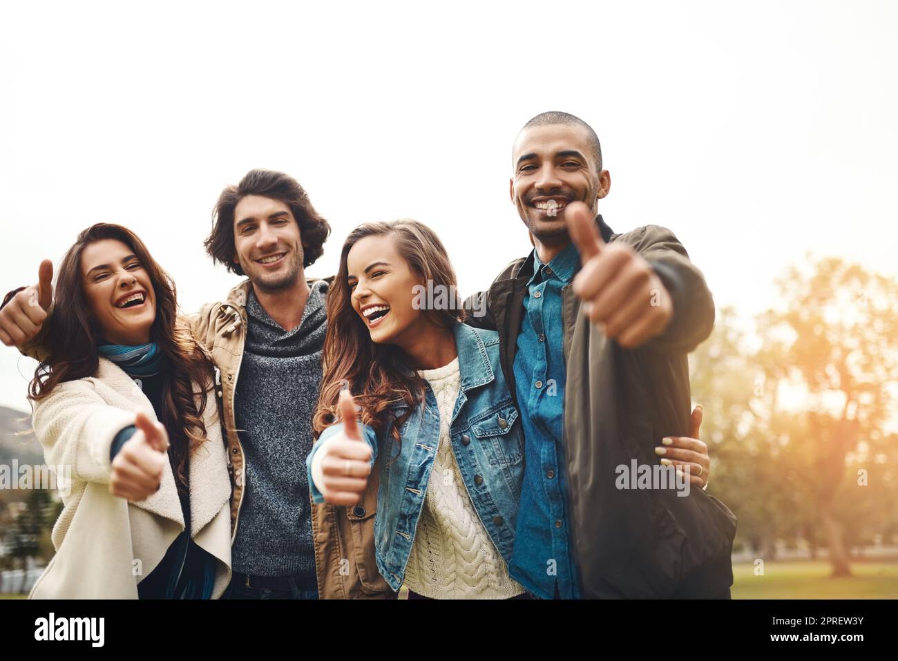 Passare del tempo con voi e' sempre speciale. Ritratto di un gruppo di allegri giovani amici che si sono rannicchiati insieme mentre si mostrano i pollici in alto durante il giorno. Foto Stock