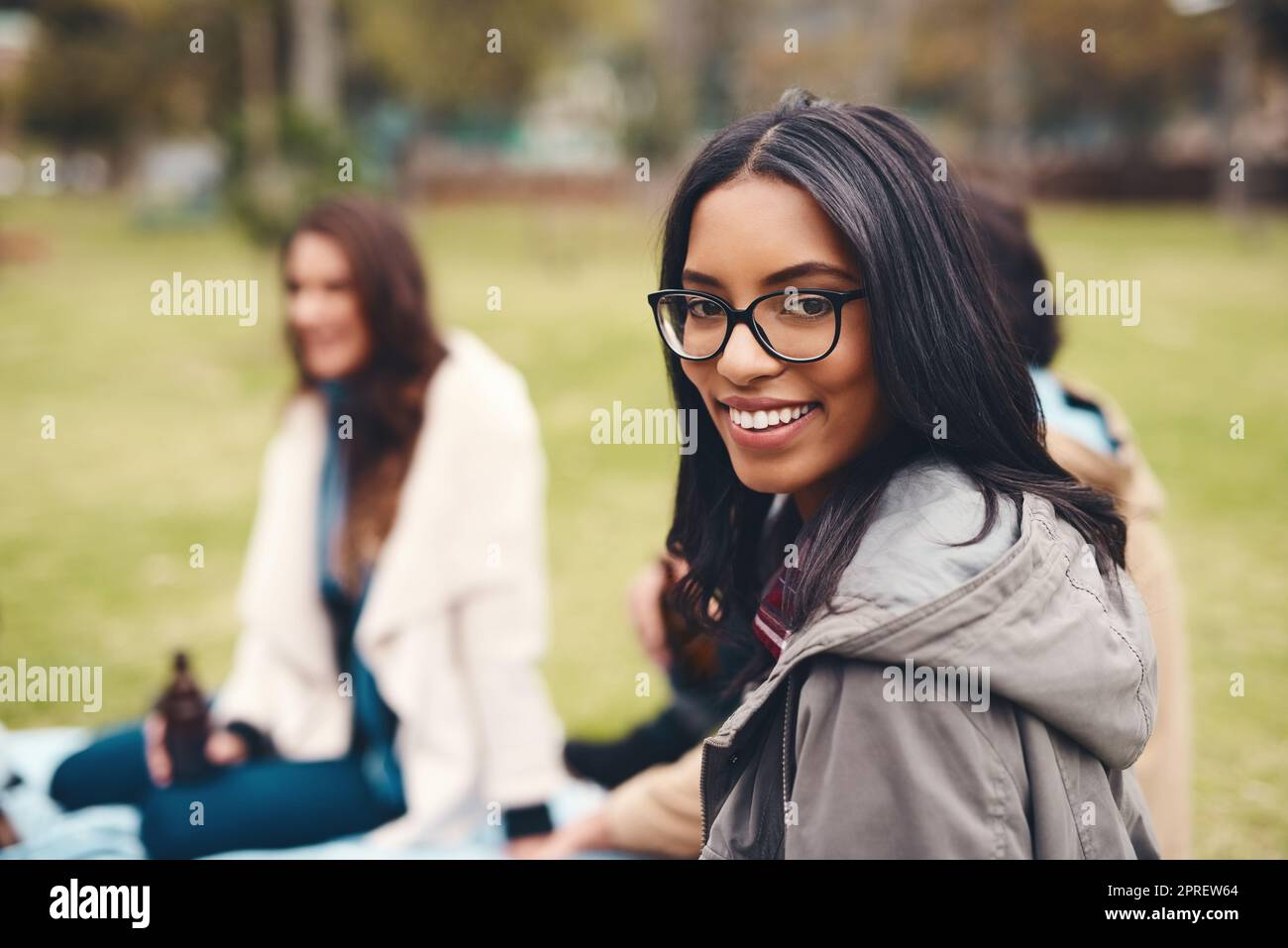 Trascorrendo la giornata semplicemente rilassandosi con i buoni amici. Ritratto di una giovane donna allegra seduta con i suoi amici in un pic-nic all'aperto durante il giorno. Foto Stock