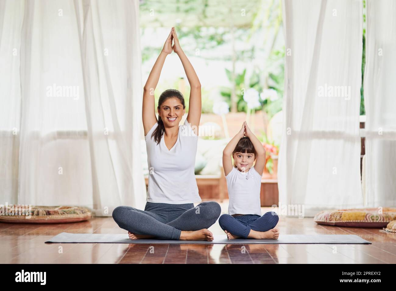 Tutti insieme ora. Ritratto di una giovane madre e figlia focalizzata che fa una posa yoga insieme alle braccia sollevate sopra la testa. Foto Stock