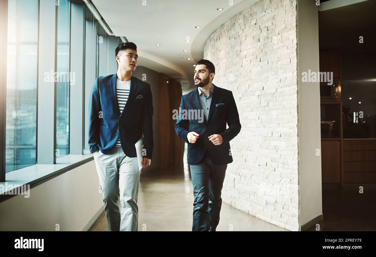 Due giovani uomini d'affari che camminano e parlano in un ufficio moderno. Foto Stock