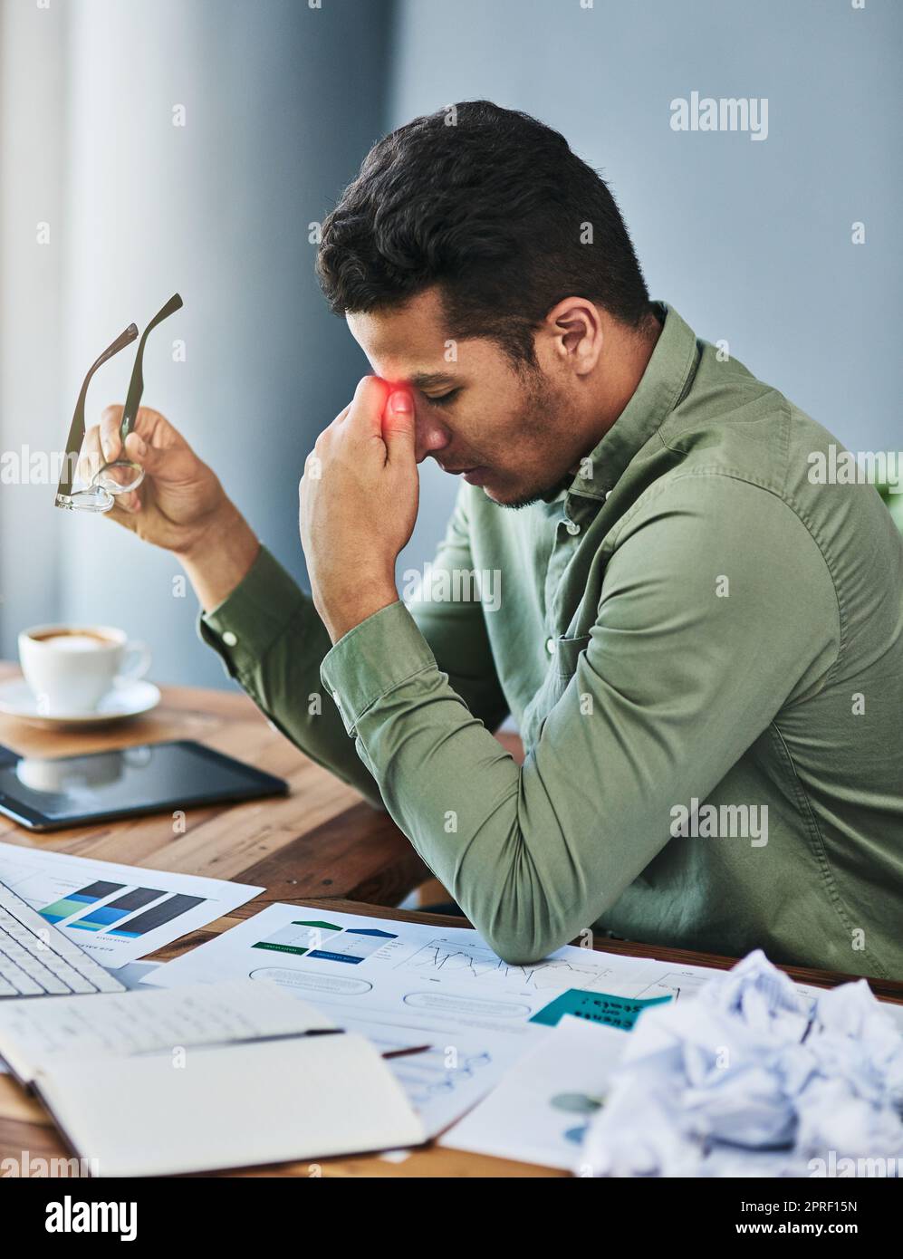 Questo mal di testa è molto irritante. un giovane uomo d'affari scomodo che tiene la fronte con la mano in difficoltà mentre è seduto alla sua scrivania in ufficio. Foto Stock