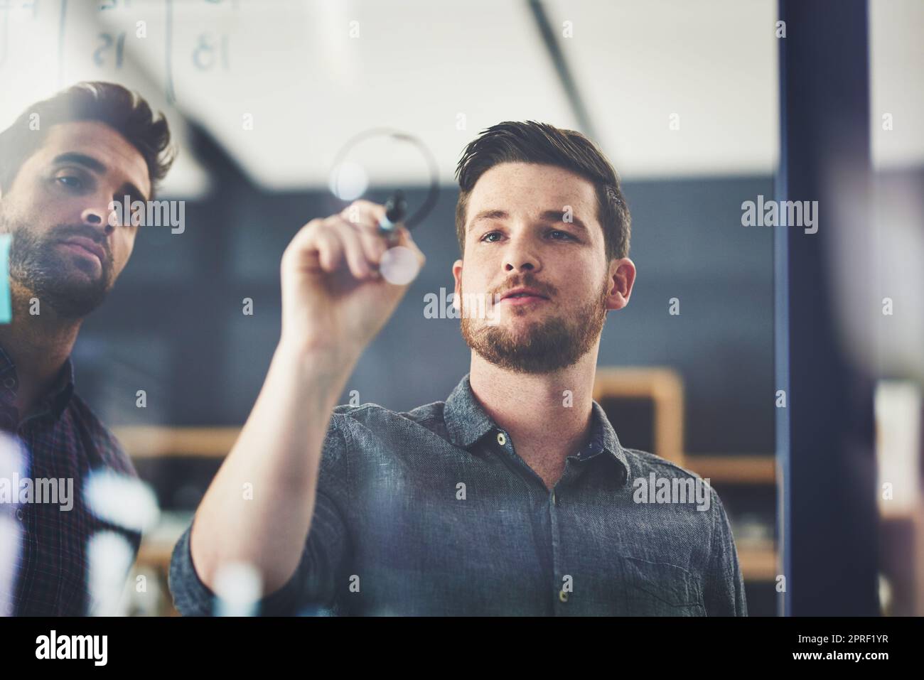 Non potete prevedere il successo senza progettarlo in primo luogo. Due giovani uomini d'affari che brainstorming su una parete di vetro in un ufficio. Foto Stock