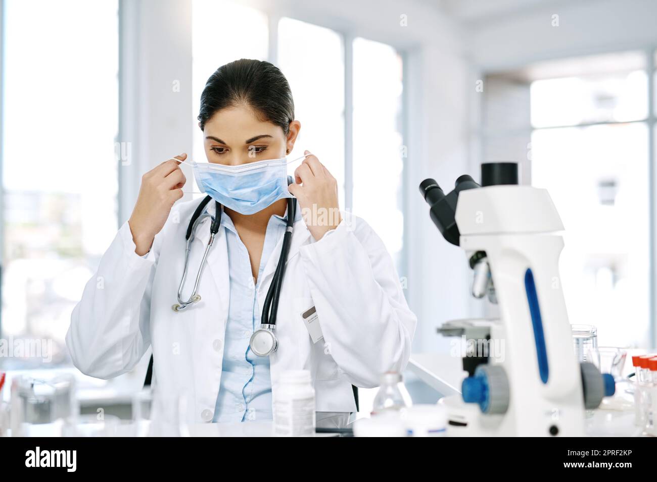 È il momento di iniziare un nuovo esperimento: Un giovane scienziato che mette una maschera chirurgica mentre lavora in laboratorio. Foto Stock