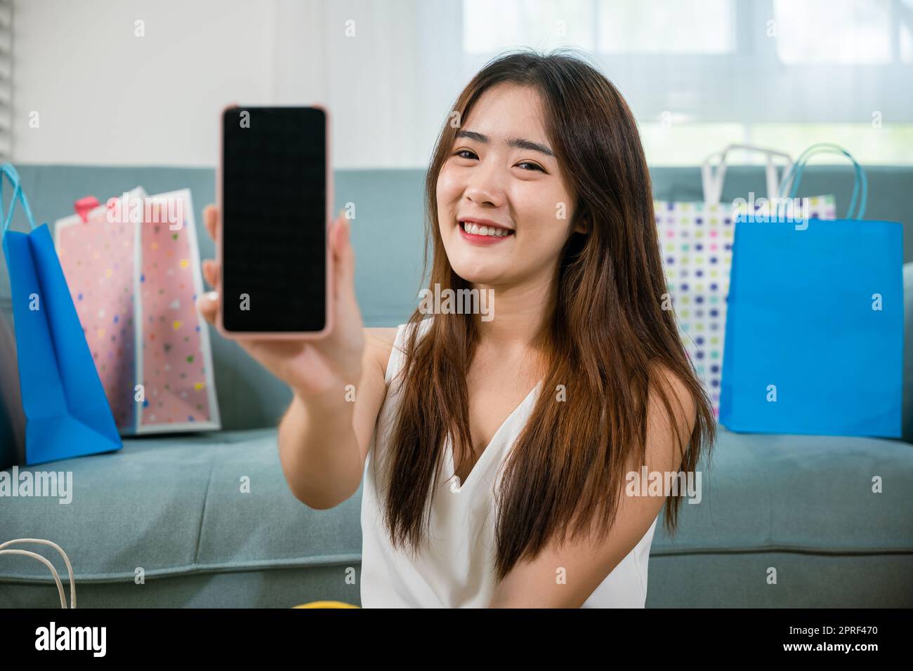Eccitato asiatico compra donna sorridente mostrando cellulare con molte borse della spesa a casa Foto Stock