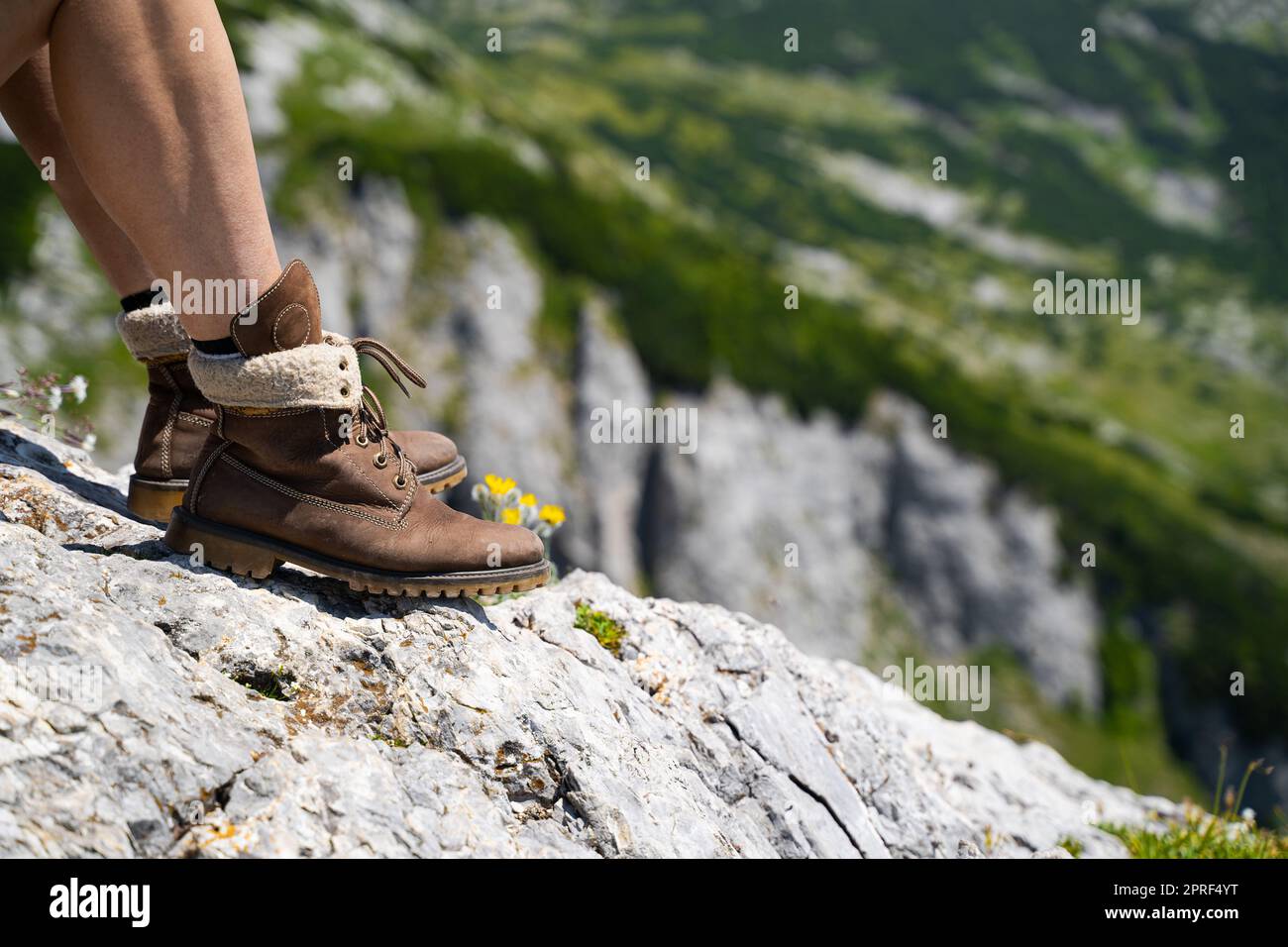 Vista laterale dettaglio primo piano delle gambe della donna caucasica con  pantaloncini di colore chiaro e stivali da trekking in pelle marrone  facendo una pausa sulla roccia di montagna Foto stock -