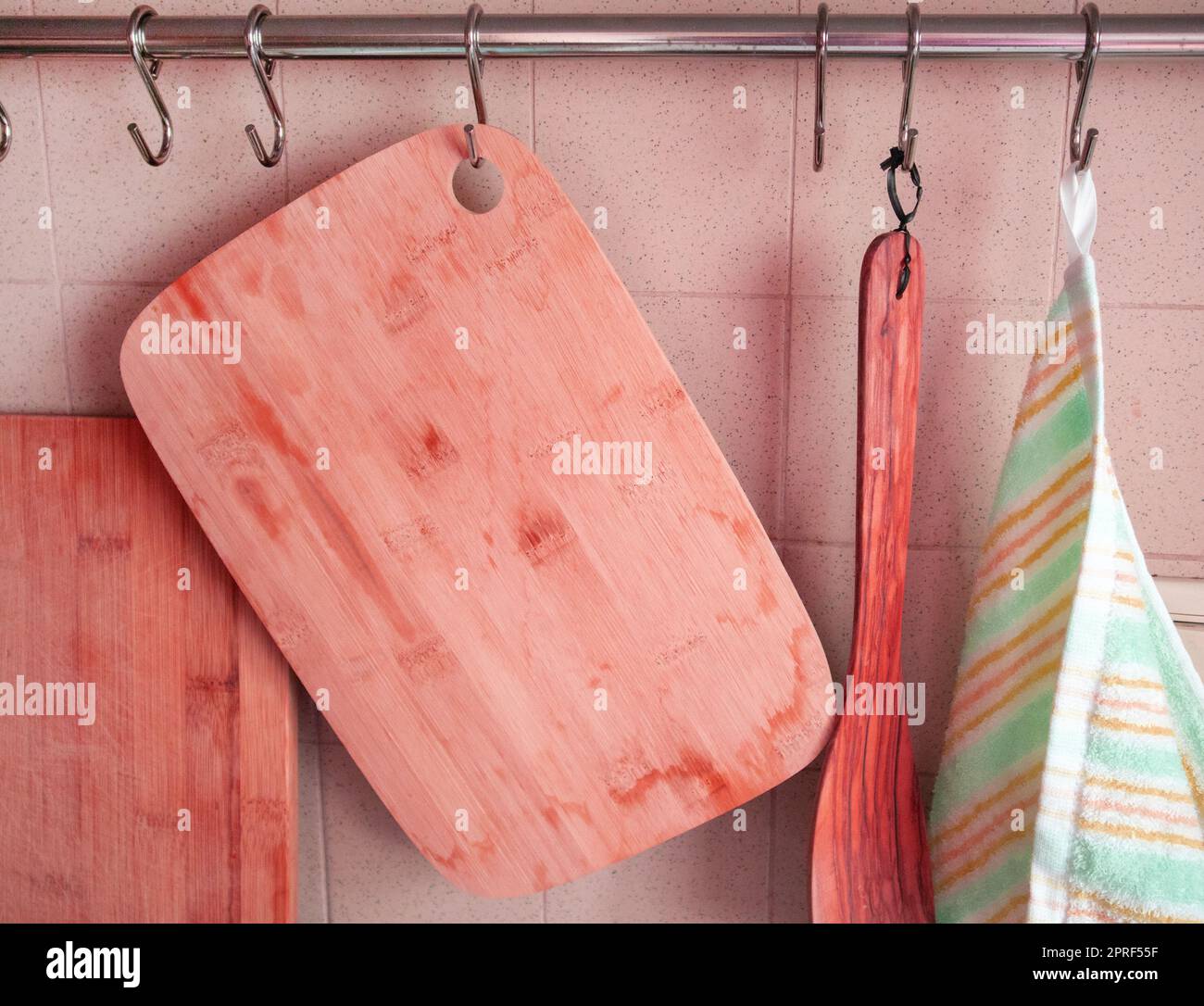 Tavole da taglio in legno, una spatola da cucina, un asciugamano da cucina appeso su ganci in cucina, sullo sfondo di una parete piastrellata, tintura rosa Foto Stock