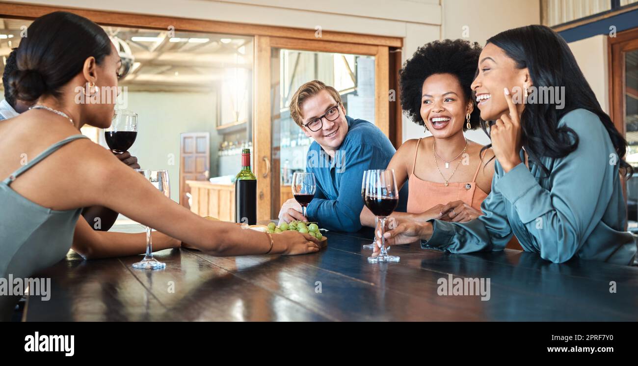 Amici sociali che bevono vino, si rilassano e parlano insieme in un ristorante per divertirsi, riunirsi e legare felici. Varietà di persone sorridenti che si divertono a conversare, mangiare e bere durante una cena Foto Stock