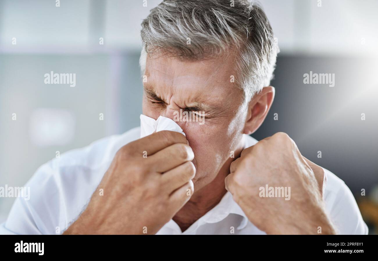 Le allergie non sono divertimento. Un uomo d'affari maturo che soffia il naso in ufficio. Foto Stock