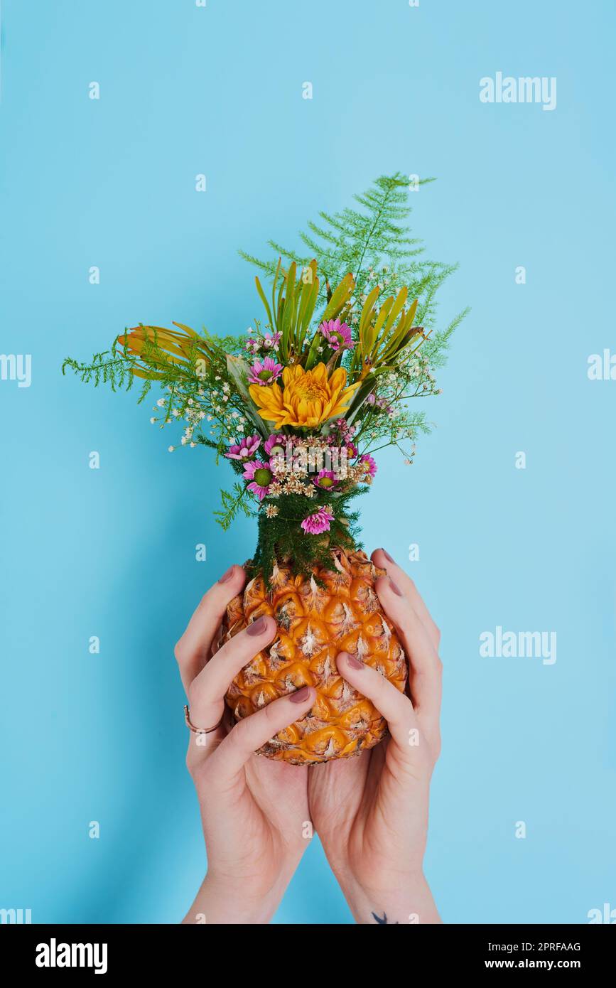 La terra ride di fiori: Una donna irriconoscibile che tiene un ananas farcito di fiori. Foto Stock