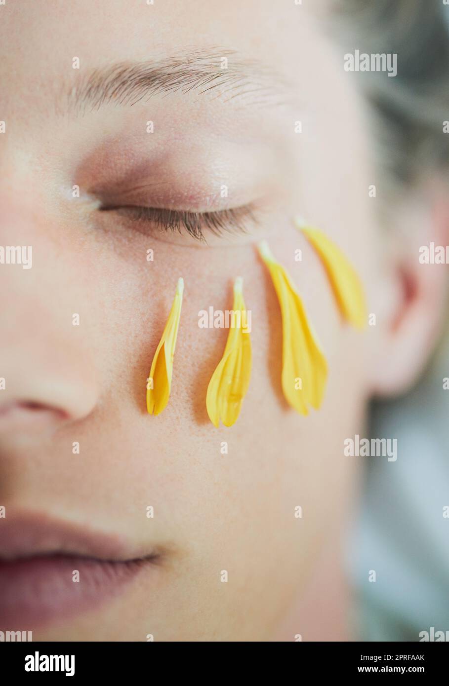 Gentile ma bello. Un giovane uomo faccia con petali di fiore sotto il suo occhio con gli occhi chiusi. Foto Stock