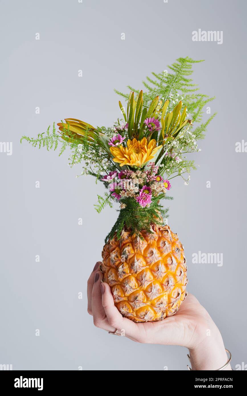Alzati, indossa una corona, essere dolce all'interno. Foto da studio di una donna irriconoscibile che tiene un ananas su uno sfondo grigio. Foto Stock