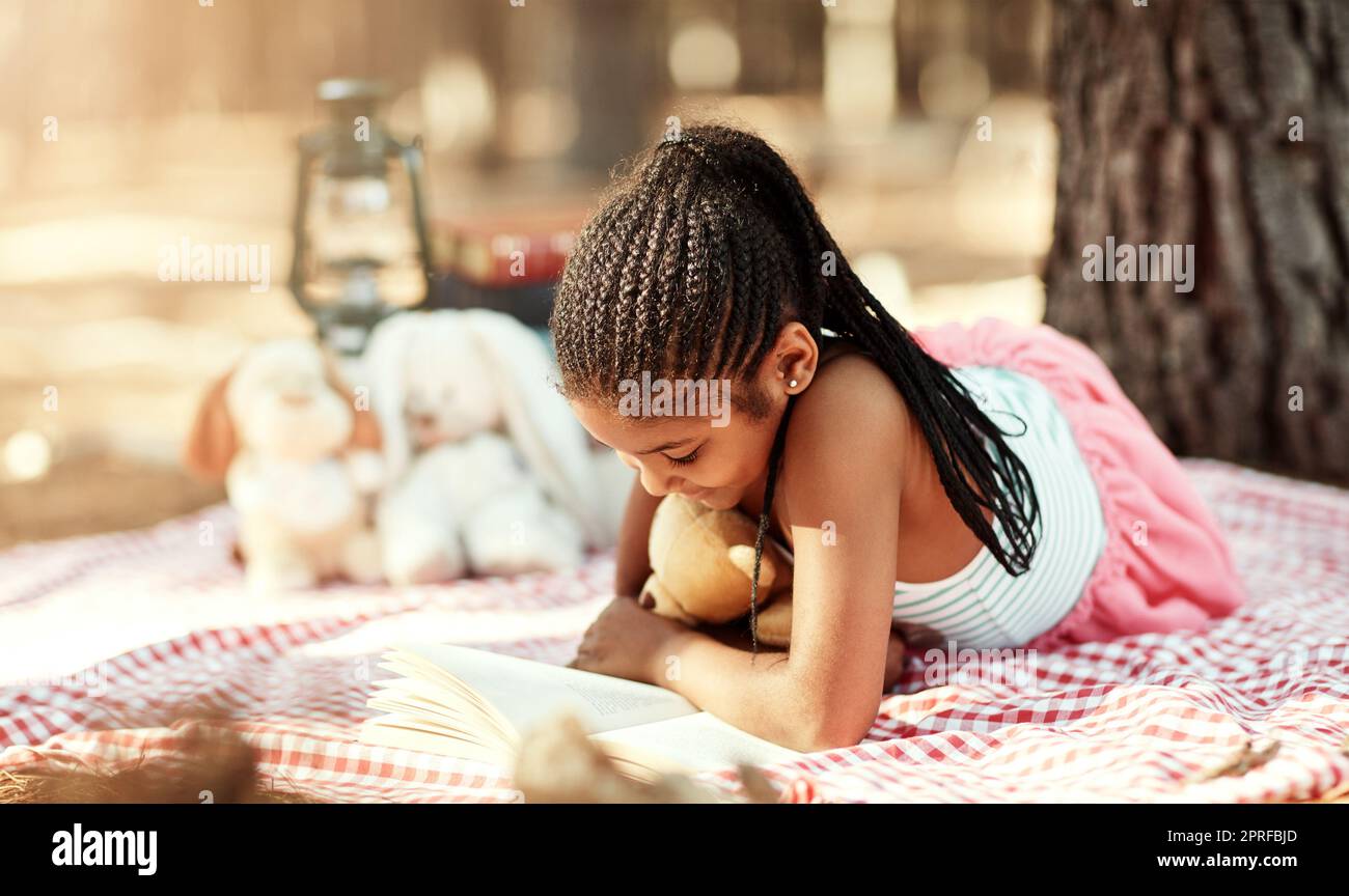 Il suo posto preferito per godere di una buona storia. Una bambina che legge un libro con i suoi giocattoli nel bosco. Foto Stock