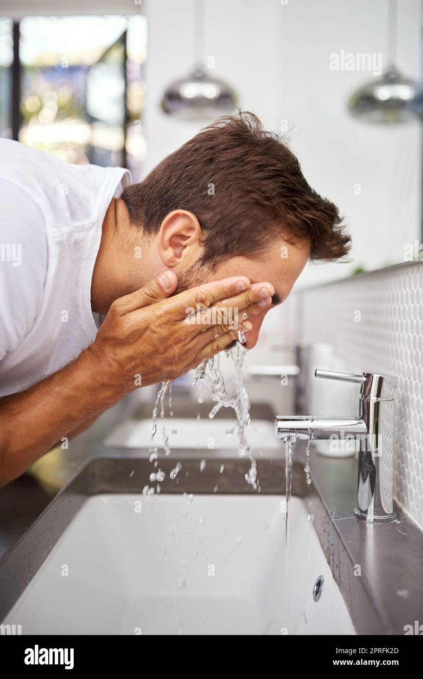 Migliore è il detergente. Immagine ravvicinata di un bell'uomo che gli spruzzi il volto con acqua nel bagno di casa. Foto Stock