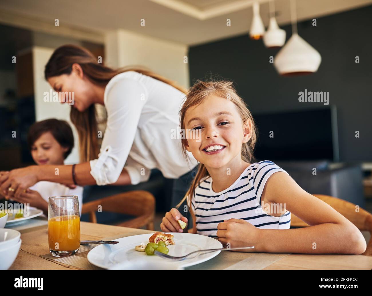 La colazione è la migliore con la mia famiglia. Ritratto di una bambina che ha fatto colazione con la sua famiglia sullo sfondo. Foto Stock