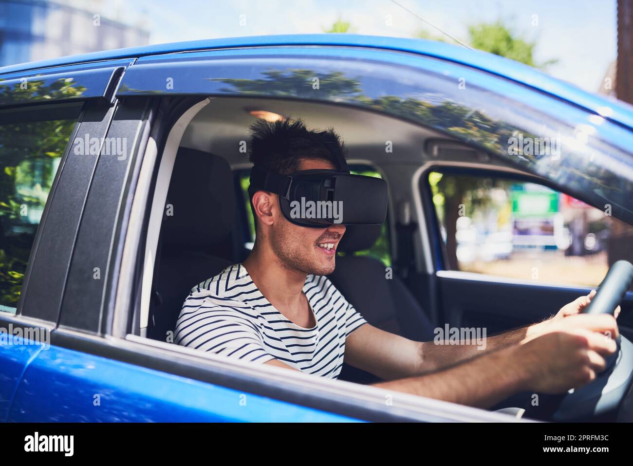 La tecnologia aggiunge un altro aspetto al viaggio: Un giovane uomo felice che guida un'auto indossando una cuffia per realtà virtuale. Foto Stock