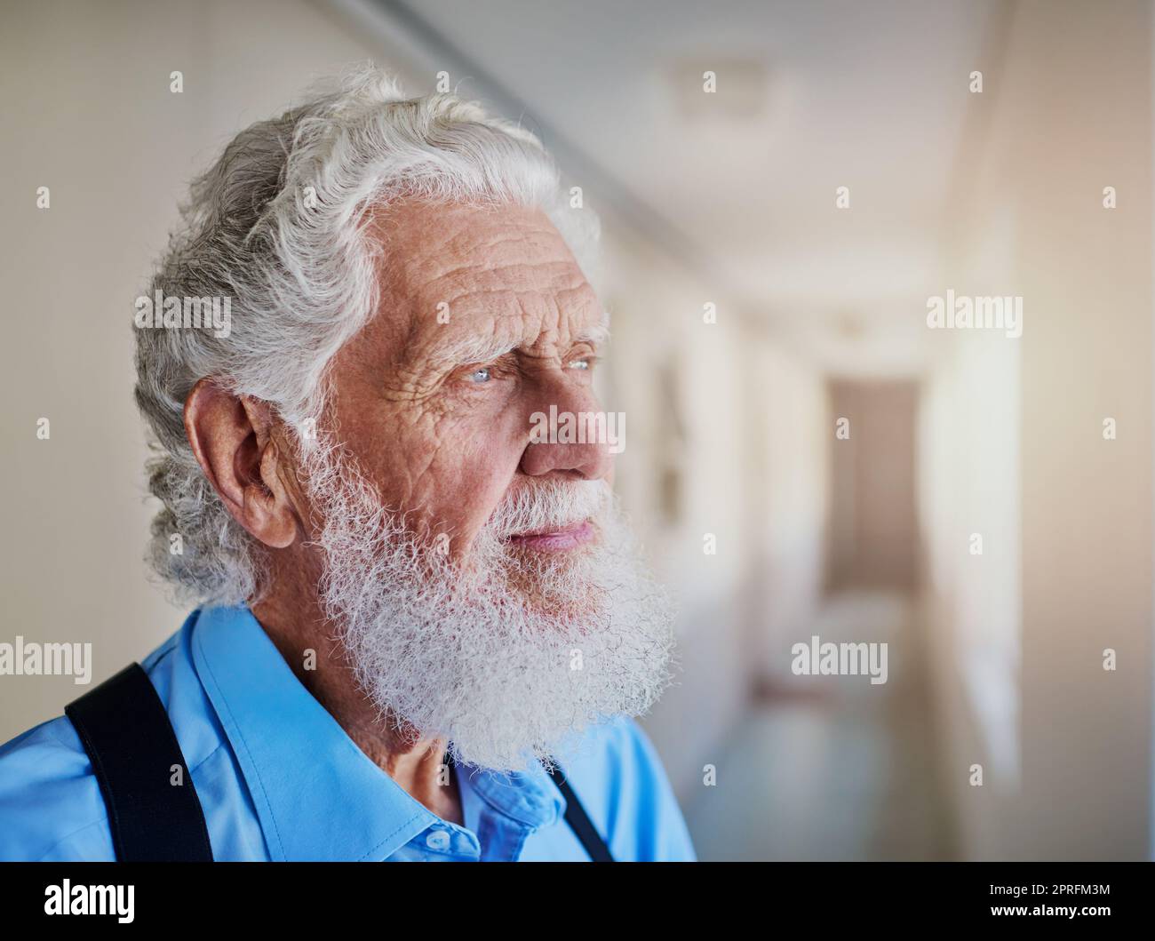 Perso nella nostalgia. Un uomo anziano che guarda premuroso mentre si trova nel corridoio della sua casa di cura. Foto Stock