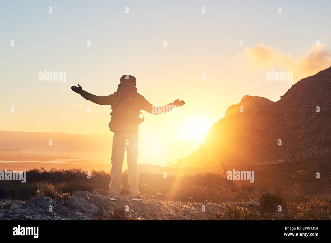 Inseguendo il sole, un escursionista con le braccia sollevate in piedi sulla cima di una montagna. Foto Stock