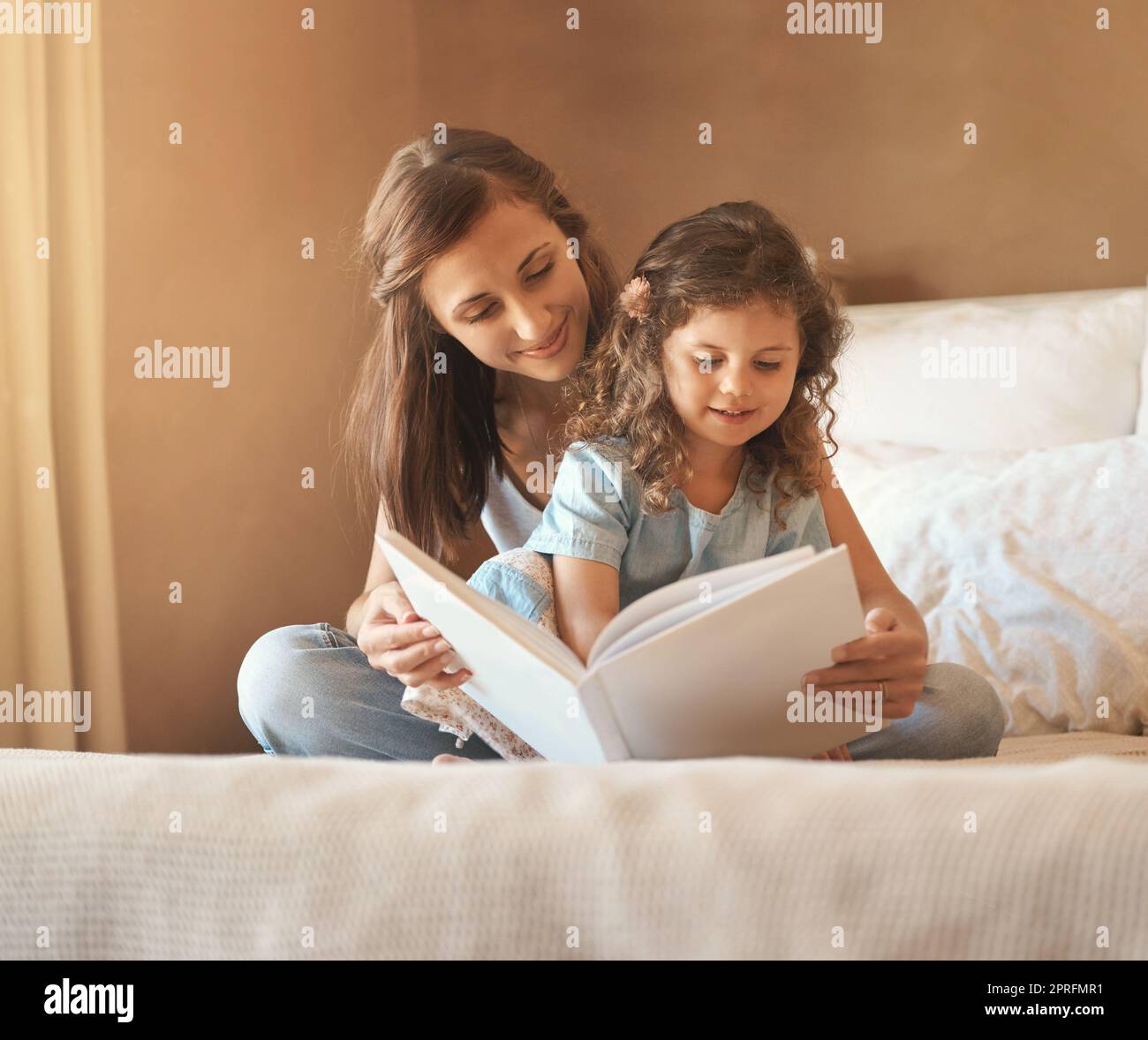 Una volta, una madre e una figlia felici a casa che leggono un libro di storia sul letto. Foto Stock