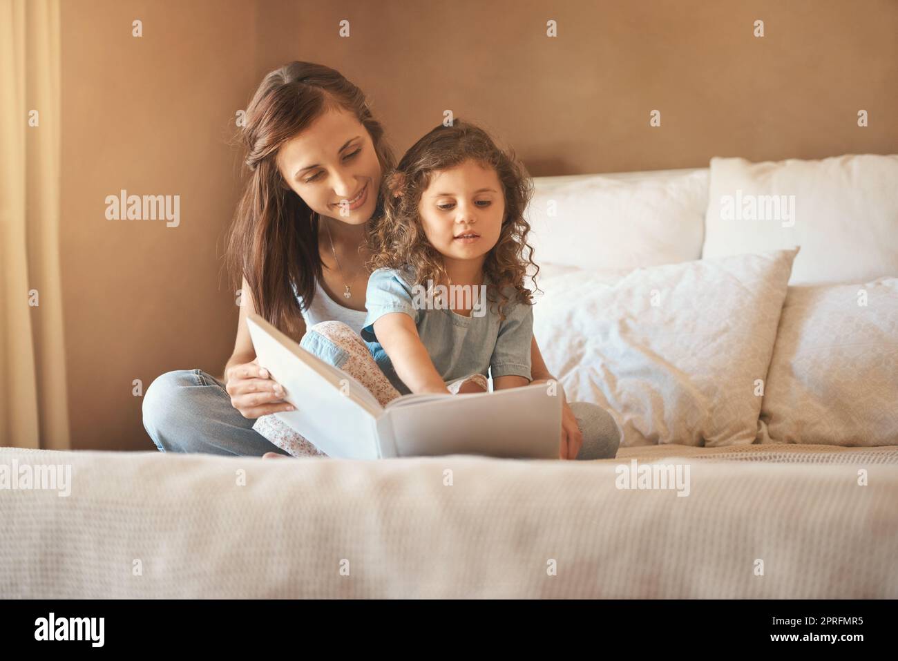 Si prega di leggere di nuovo mommy. Una madre felice e figlia a casa a leggere un libro di storia sul letto. Foto Stock