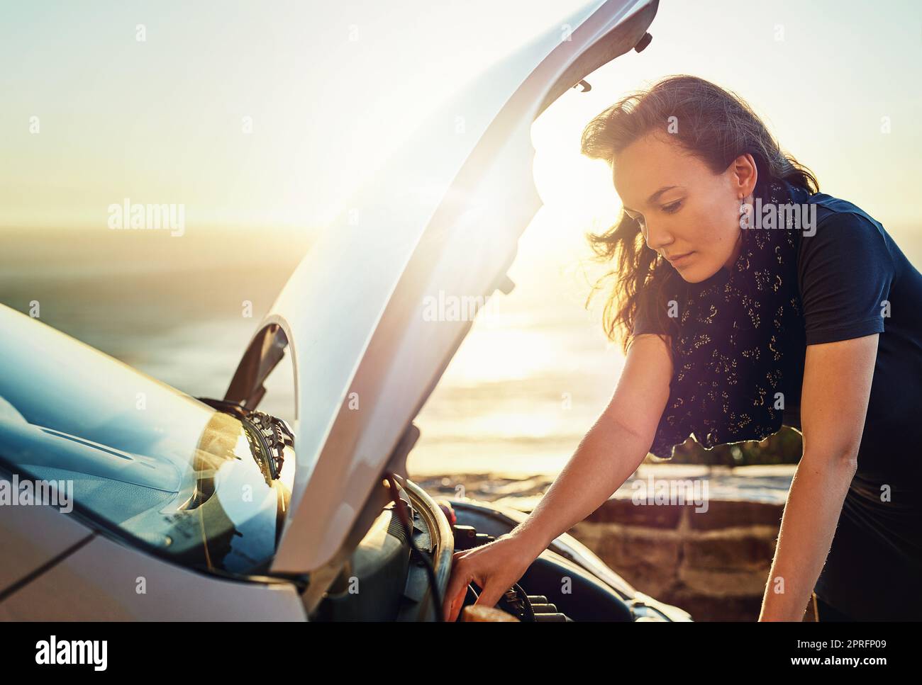 Quale potrebbe essere il problema...una giovane donna che controlla sotto il cofano della sua auto dopo la rottura sulla strada. Foto Stock