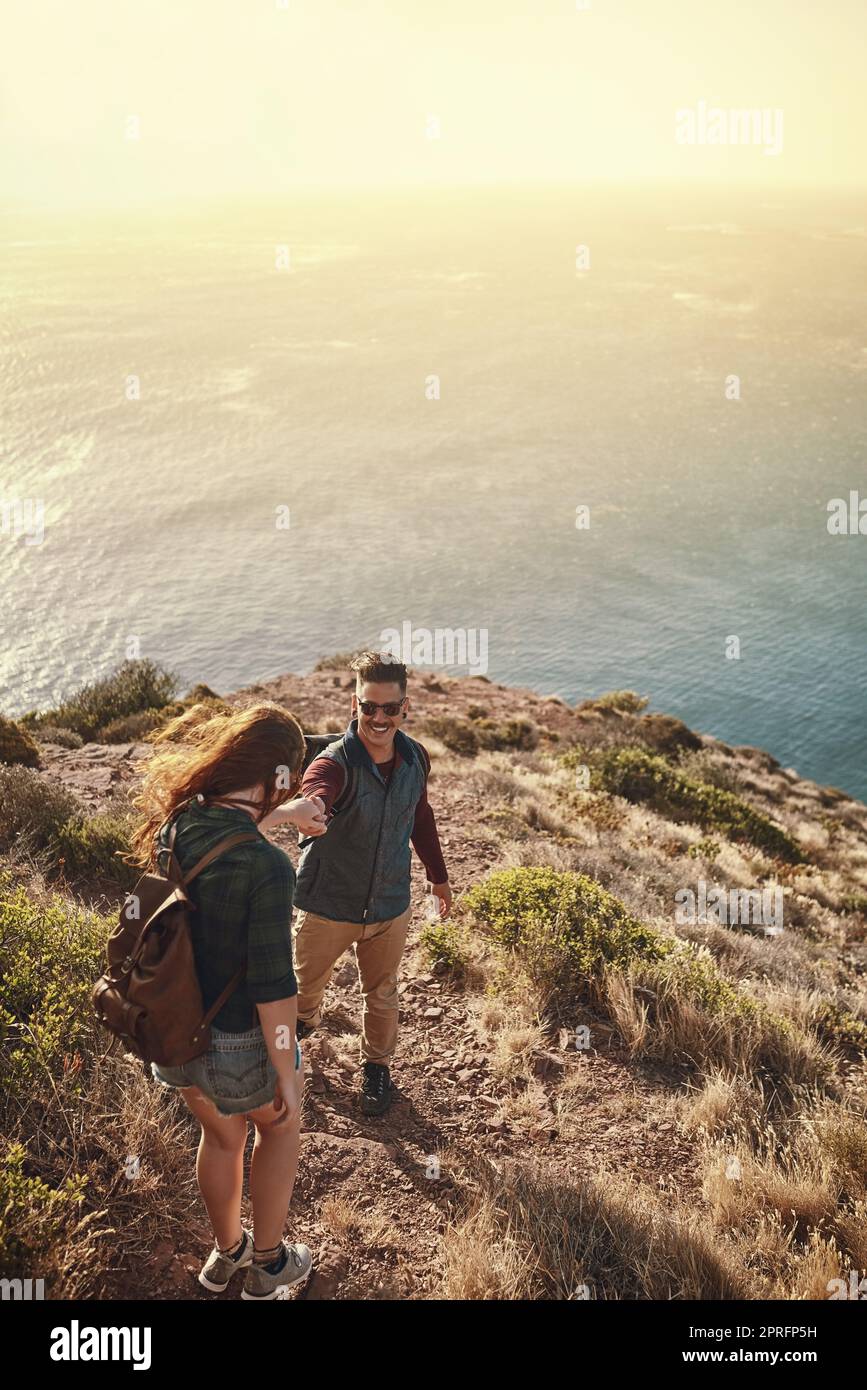 Permettetemi di darti una mano. Colpo ad angolo alto di un giovane che aiuta la sua ragazza mentre camminano attraverso le montagne. Foto Stock