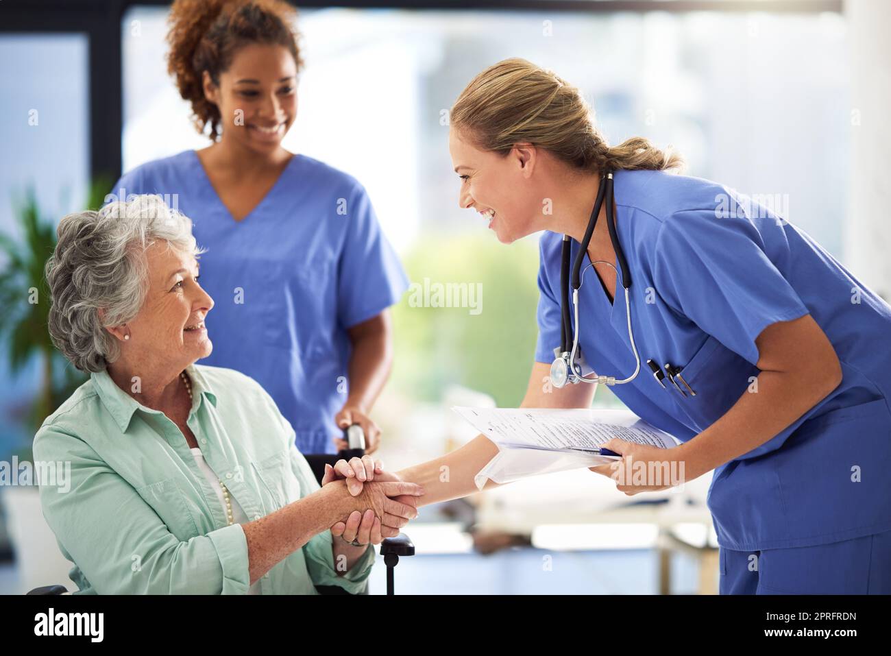 Si assicura che riceva il miglior aiuto che merita. un medico in possesso di cartelle cliniche e stringendo la mano con una donna anziana sorridente seduta su una sedia a rotelle. Foto Stock