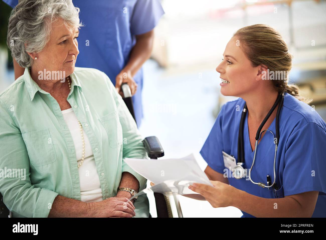 Un medico che discute i trattamenti con una donna anziana seduta in sedia a rotelle in un ospedale. Foto Stock