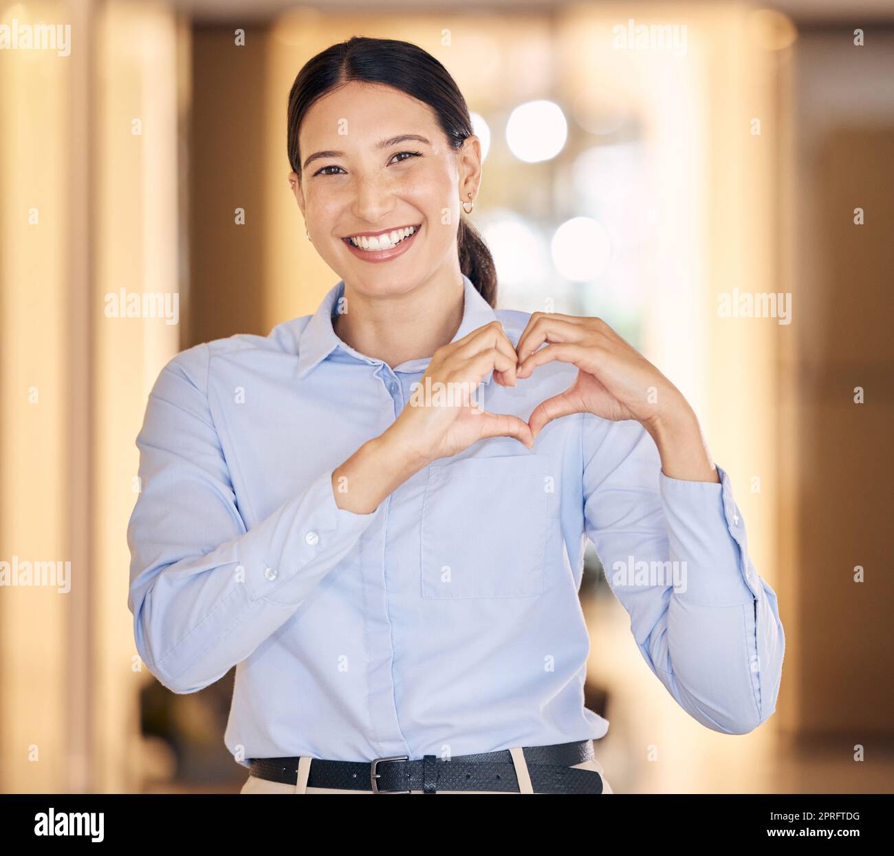 Donna d'affari con emoji amore e segno del cuore o mano in ritratto con sorriso e bokeh. Persona aziendale professionale o dipendente felice con mani positive, curate e fiduciarie icona per la felicità della carriera Foto Stock