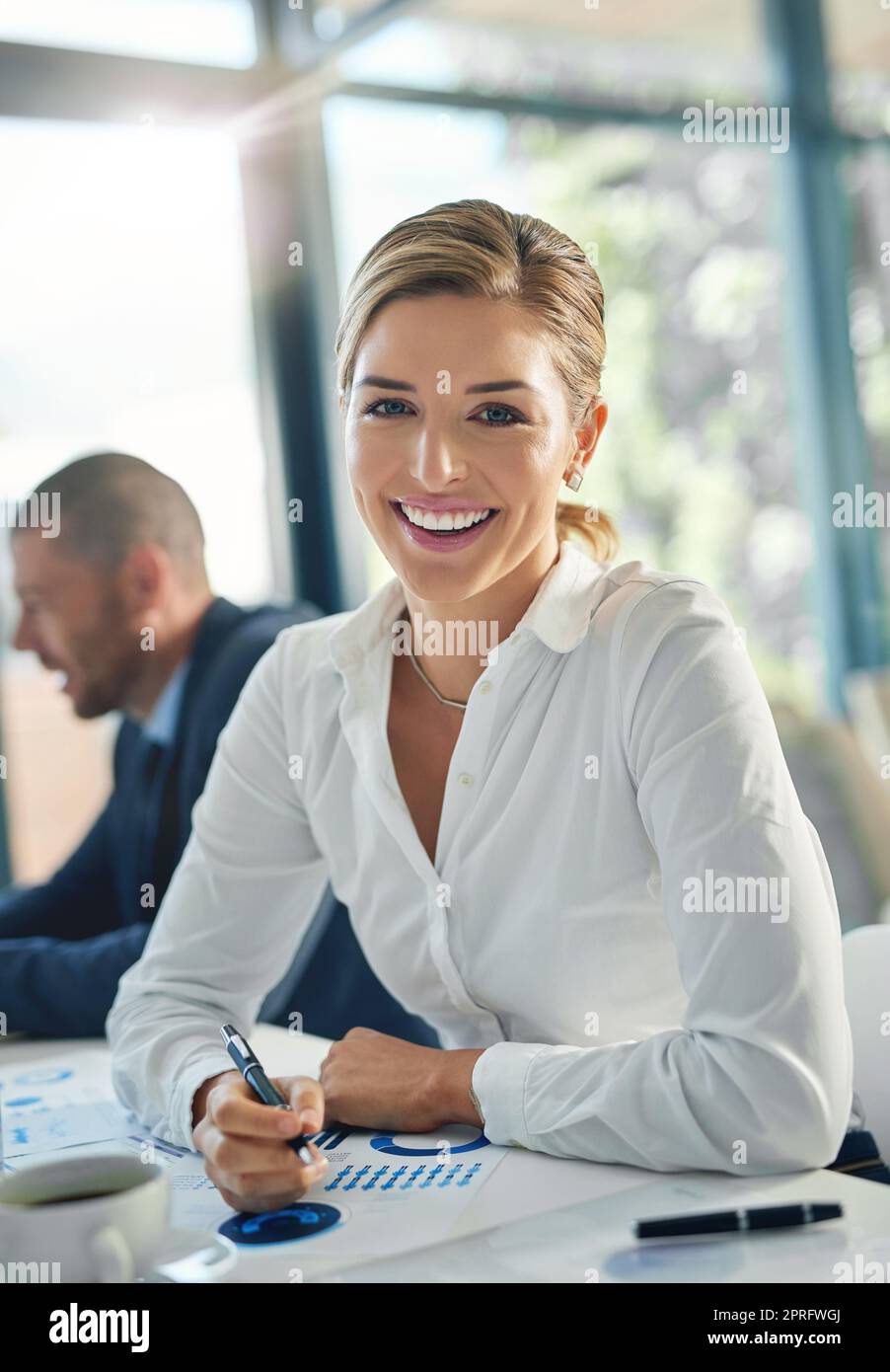 Una volta realizzato il vostro scopo, lavori duro per realizzarlo. Ritratto di una giovane donna d'affari seduta in ufficio con la sua collega sullo sfondo. Foto Stock