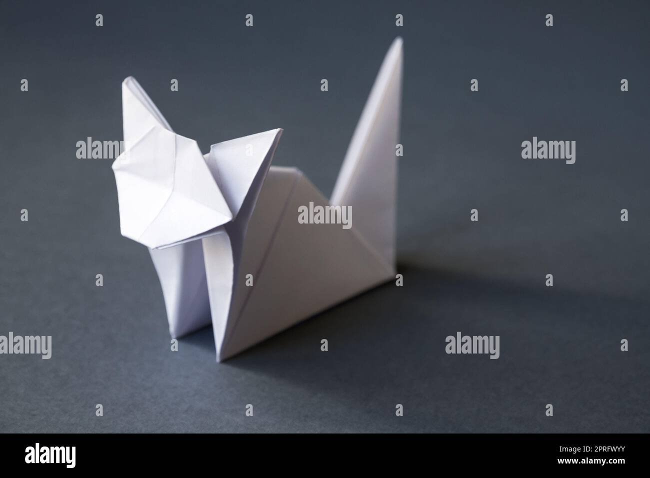 Carta bianca gatto origami isolato su uno sfondo grigio Foto Stock