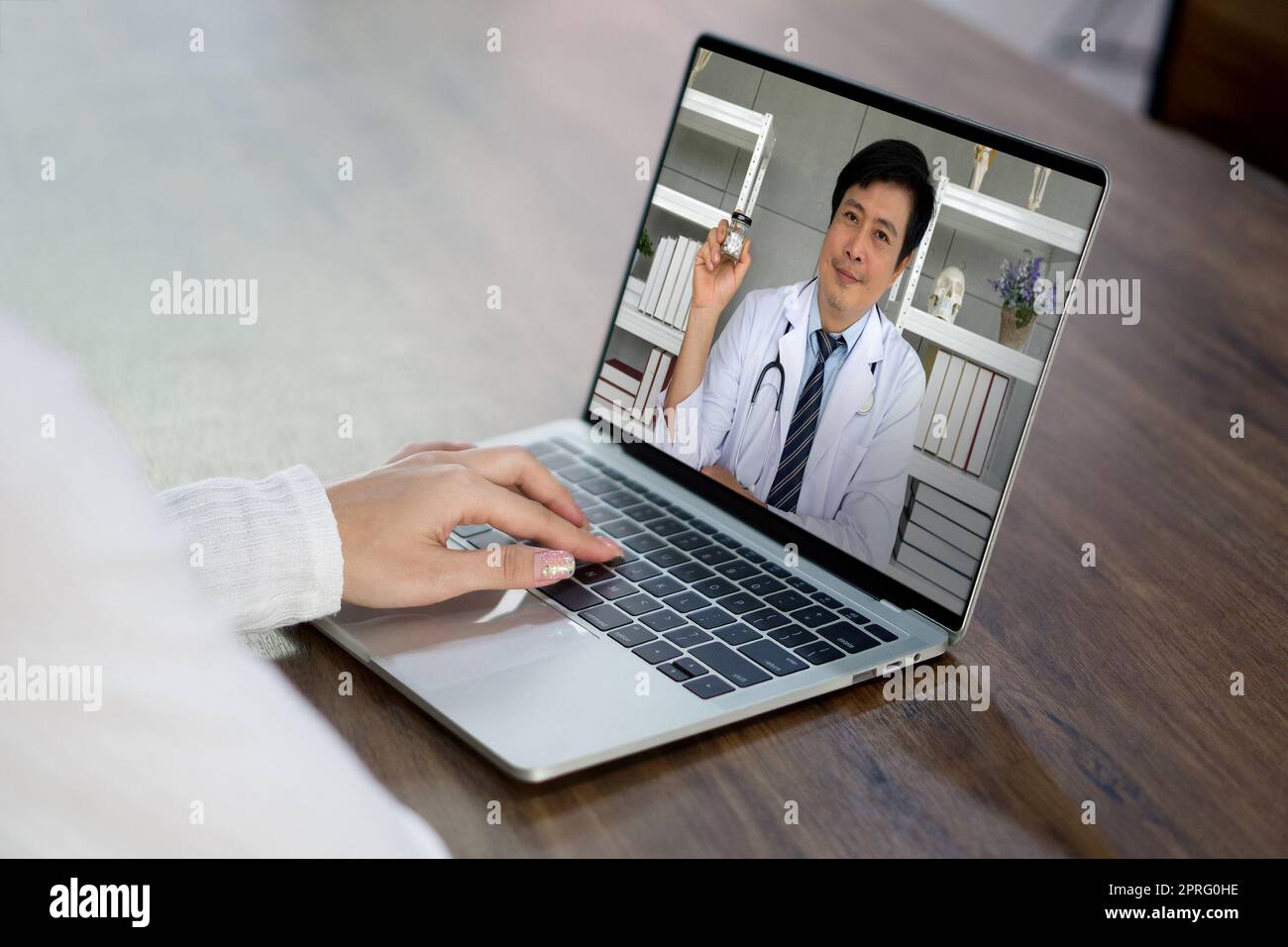 Vista posteriore della donna sedersi alla scrivania a casa avere conferenza webcam sul computer portatile con il medico asiatico circa capsula medica. Concetto di sanità e medicina. Foto Stock