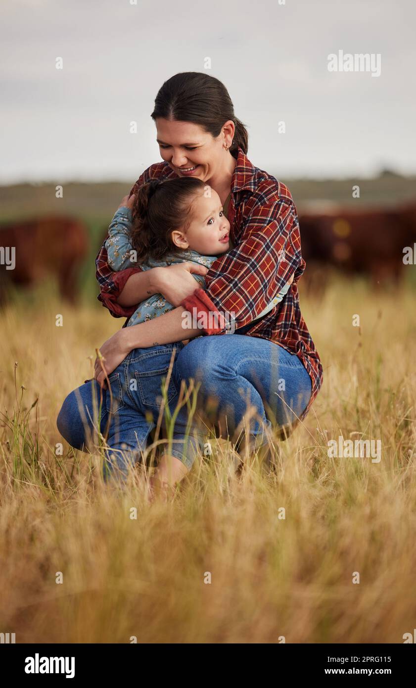 Amore, famiglia e cura con una madre e una figlia che abbracciano in un campo all'aperto in una fattoria. Allevatore di bestiame e bambina nell'industria agricola, agricola e lattiero-casearia su un prato o pascolo all'aperto Foto Stock