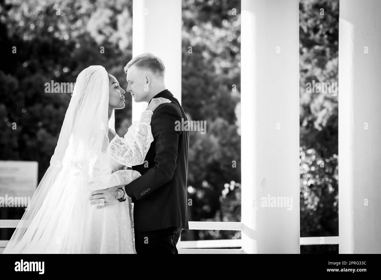 Sposi novelli a razza mista in una passeggiata che abbraccia e guarda amorevolmente l'un l'altro, fotografia in bianco e nero Foto Stock