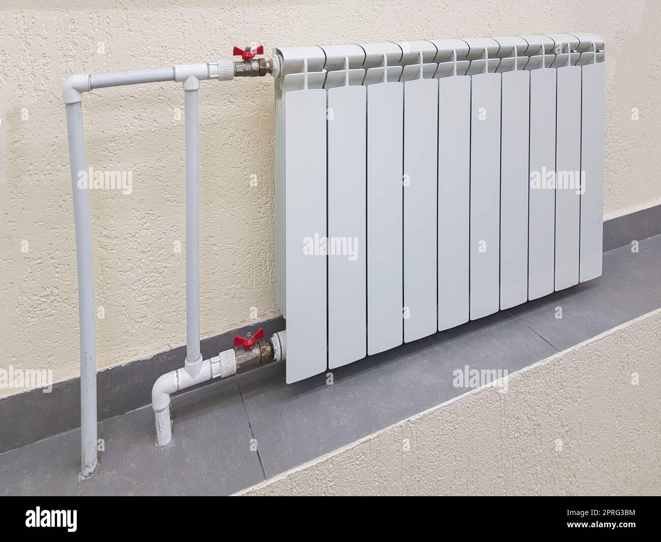 Batteria bianca per radiatore in alluminio moderno per riscaldamento ad acqua calda, sullo sfondo di una parete all'interno di un appartamento o di un ufficio Foto Stock
