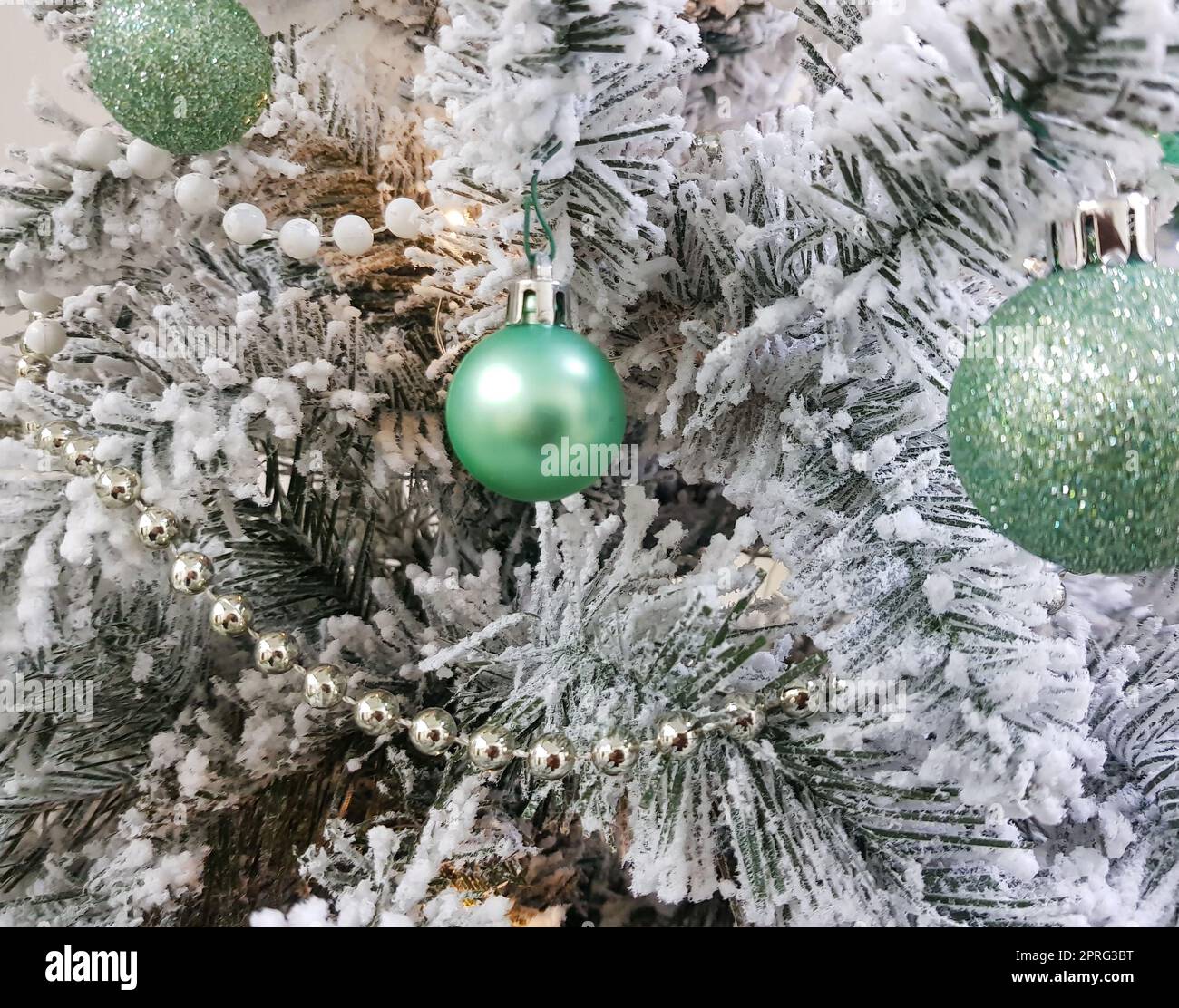 Palline verdi lucenti sull'albero di Natale. Perle bianche sui rami di abete rosso. I rami sono ricoperti di ghiaccio. Sfondo natalizio o capodanno Foto Stock