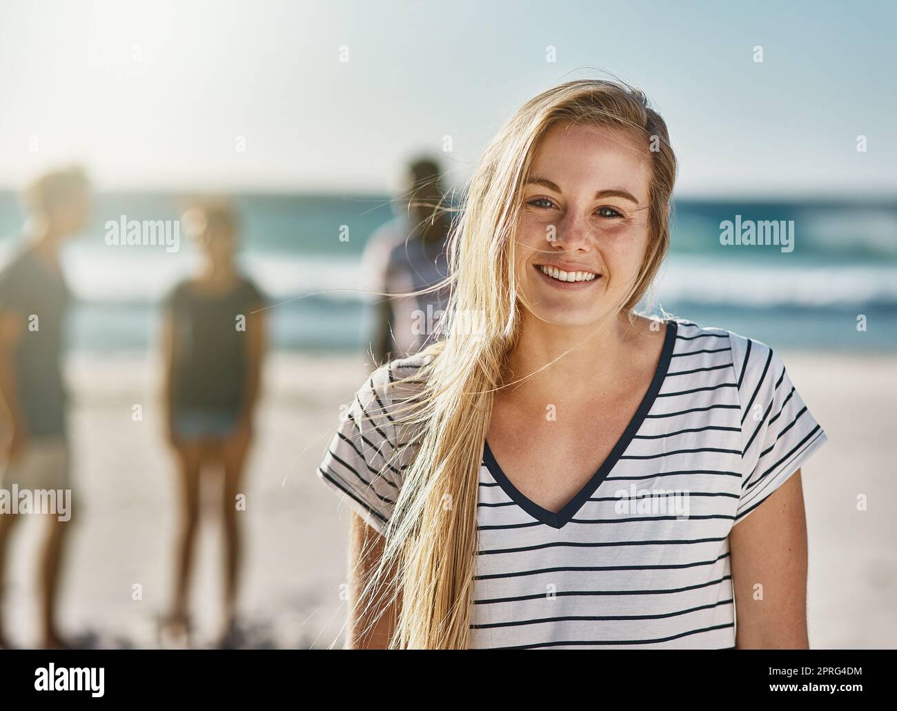 Non dico mai di no ad una giornata in spiaggia. Ritratto di una giovane donna felice che si posa sulla spiaggia con i suoi amici sullo sfondo. Foto Stock