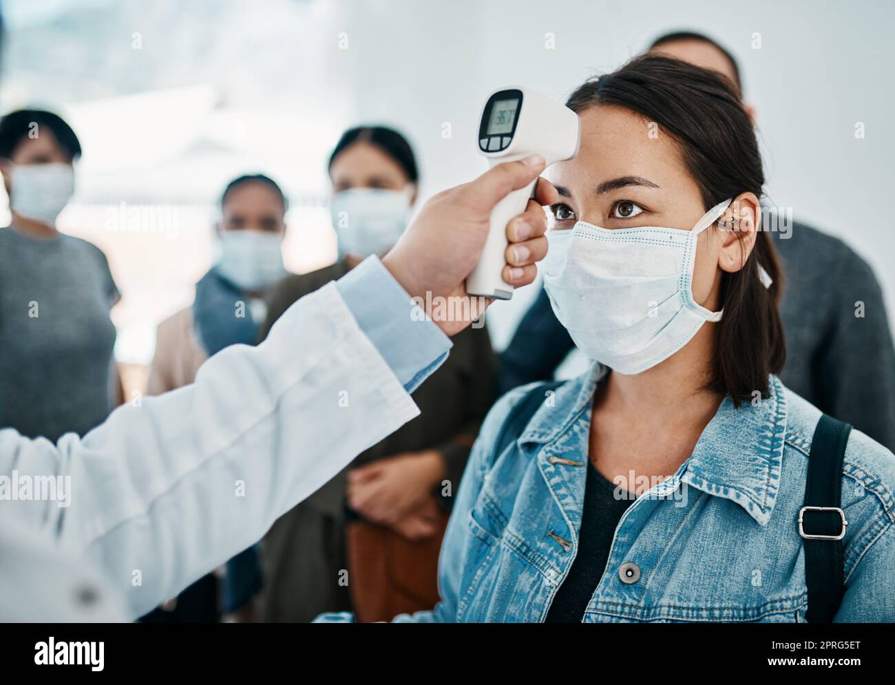 Screening COVID con una turista femminile in maschera che ha preso la sua temperatura con un termometro a infrarossi mentre aspetta di salire a bordo in un aeroporto. Restrizioni di viaggio durante la pandemia del virus della corona Foto Stock