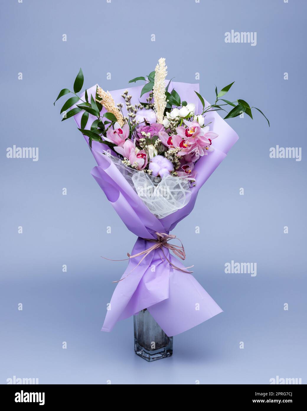 Bouquet di ingredienti naturali avvolti in carta da ricalco floreale, si staglia in vaso su sfondo blu. Foto Stock