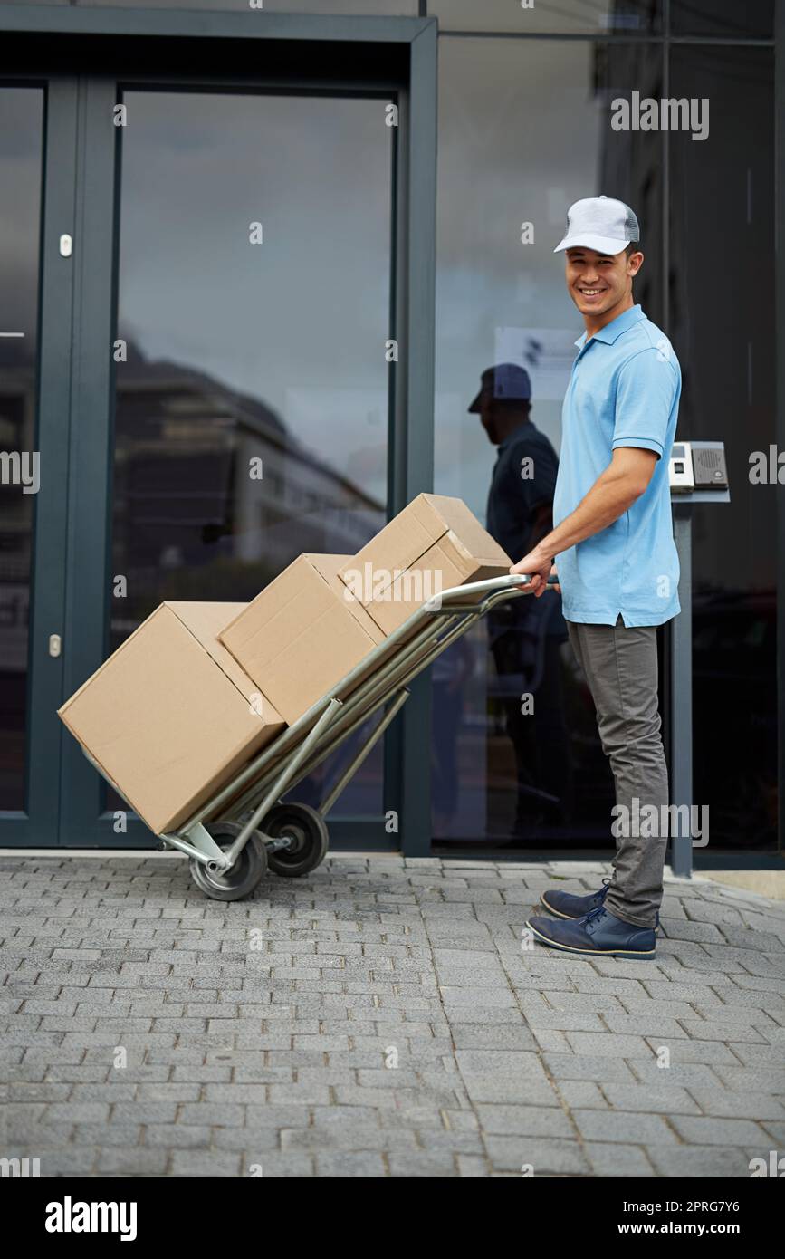 Bene, tutto ti viene consegnato. Ritratto di un corriere che spinge un carrello di scatole durante la consegna. Foto Stock