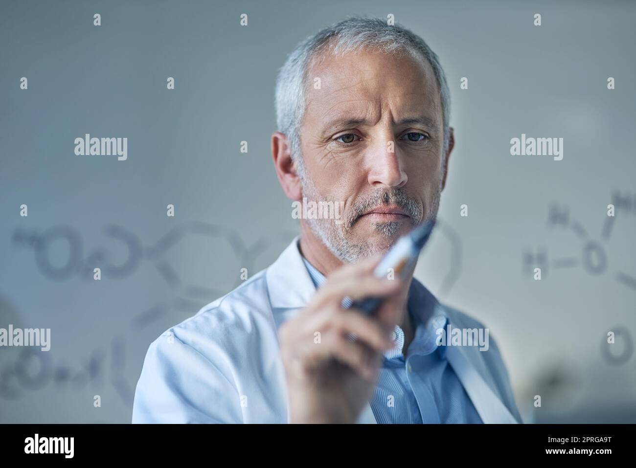 Figurando i suoi risultati. Uno scienziato maschio che disegna strutture molecolari su una parete di vetro in un laboratorio. Foto Stock