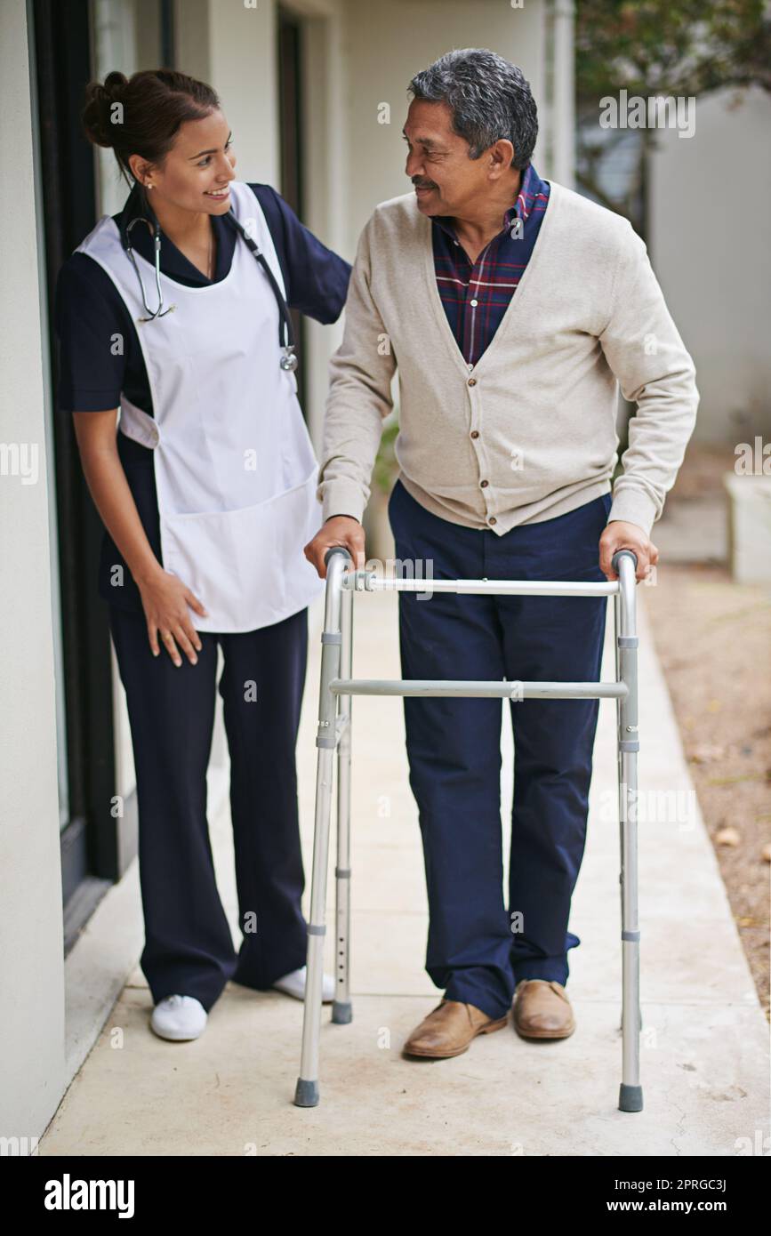 Insieme ogni passo del modo. Un'infermiera che va per una passeggiata con il suo paziente anziano e il suo camminatore in una casa di riposo. Foto Stock