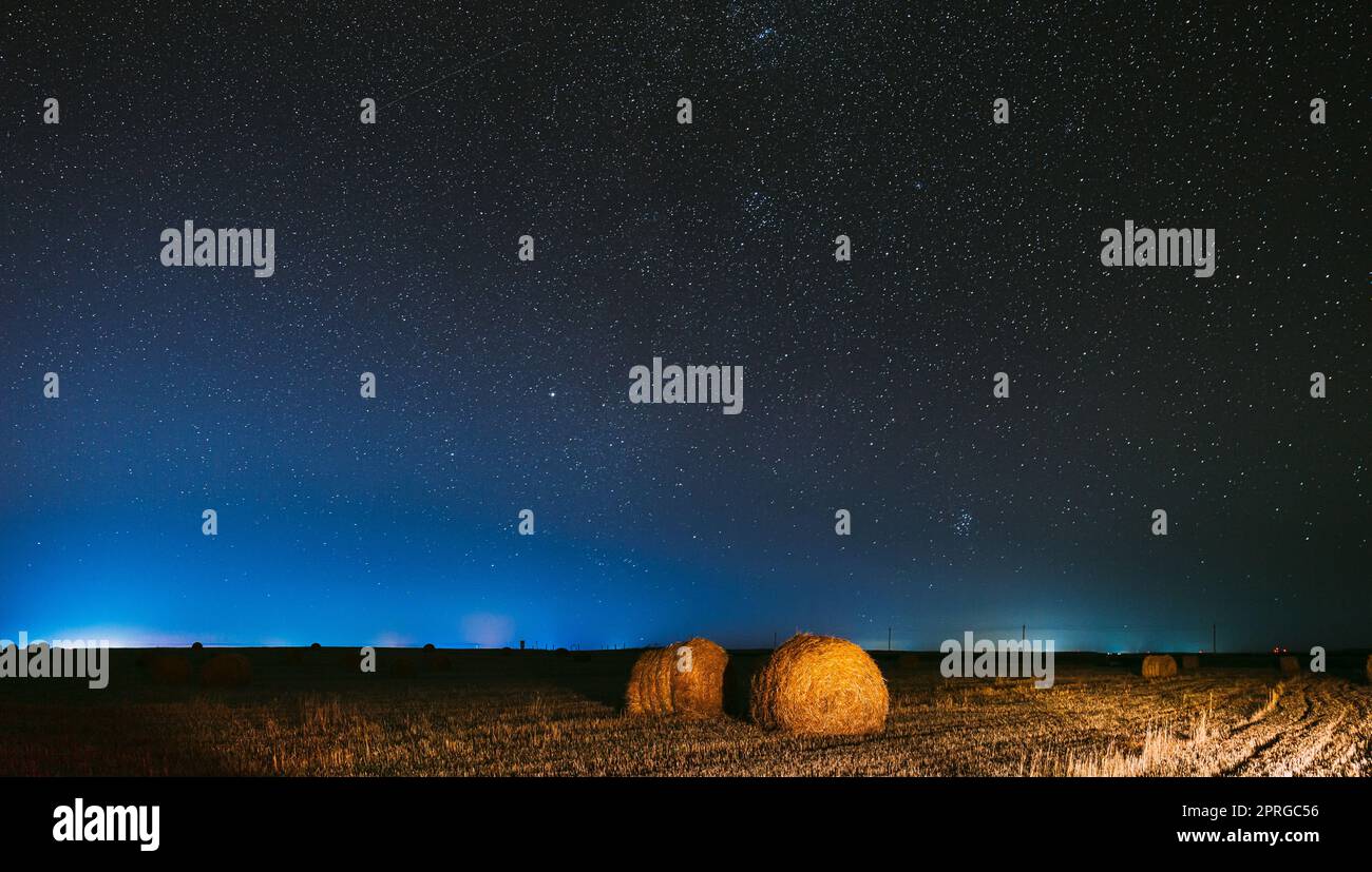 Cielo stellato di notte sopra Haystack nel campo agricolo estivo. Notte Stelle sopra il paesaggio rurale con balle di fieno dopo Harvest. Panorama agricolo Foto Stock