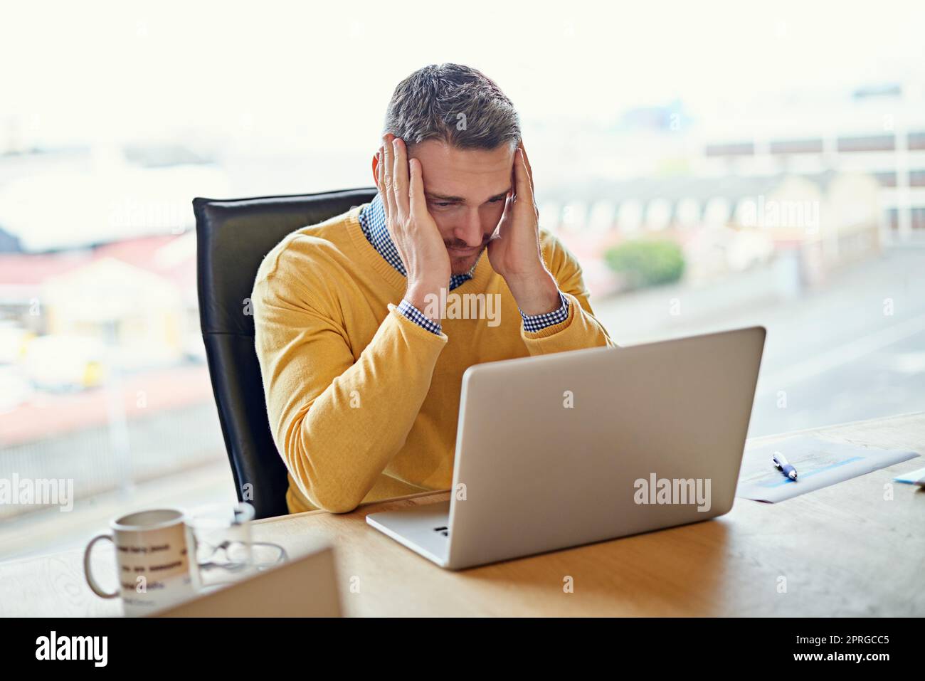 Giornata stressante in ufficio. Immagine di un uomo d'affari che lavora sul suo computer portatile alla sua scrivania. Foto Stock
