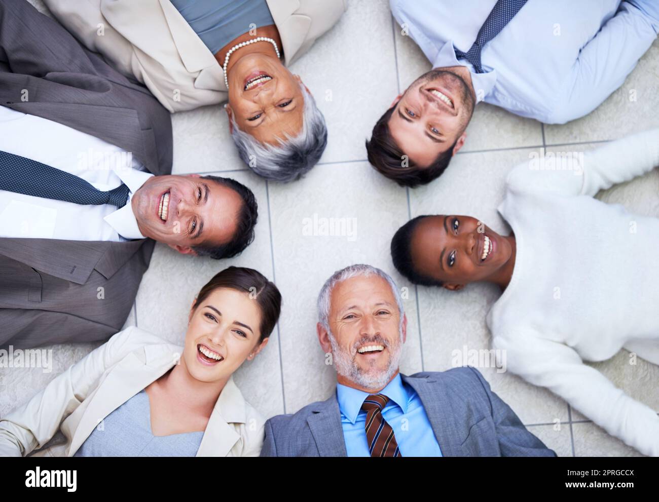 È importante avere buoni rapporti di affari. Ritratto ad angolo alto di un gruppo di uomini d'affari diversi che giacciono sul pavimento in un cerchio. Foto Stock