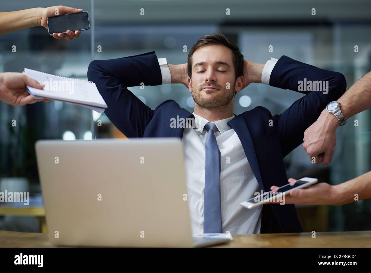 Affrontare le esigenze aziendali con calma. Immagine di un uomo d'affari seduto tranquillamente alla sua scrivania mentre circondato da colleghi esigenti in un ufficio. Foto Stock